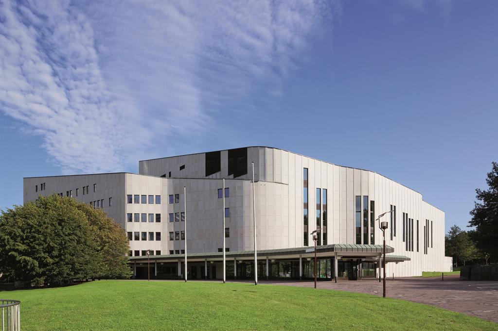 Modernes, weißes Gebäude mit großen Fenstern vor grünem Rasen und blauem Himmel
