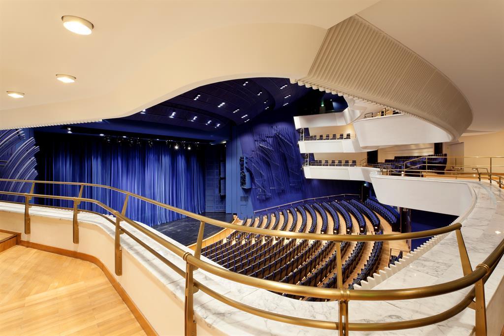 Innenansicht eines Theatersaals mit blauen Vorhängen, geschwungenen Sitzreihen und goldfarbenen Geländern