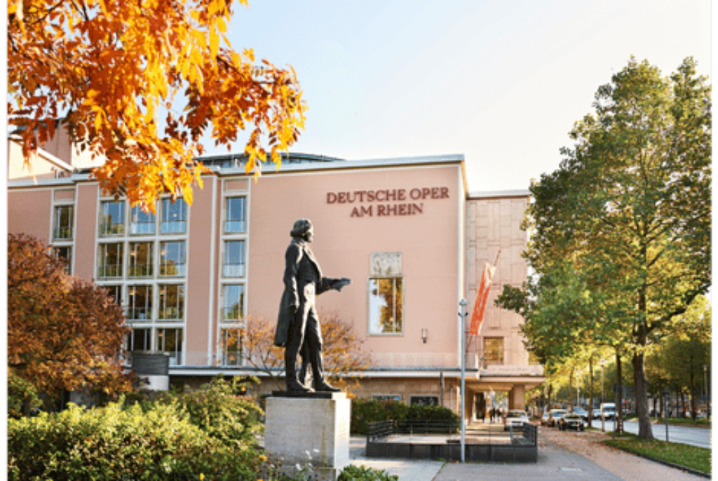 Statue vor dem Gebäude der Deutschen Oper am Rhein in Düsseldorf mit herbstlich gefärbten Bäumen und einer Allee daneben