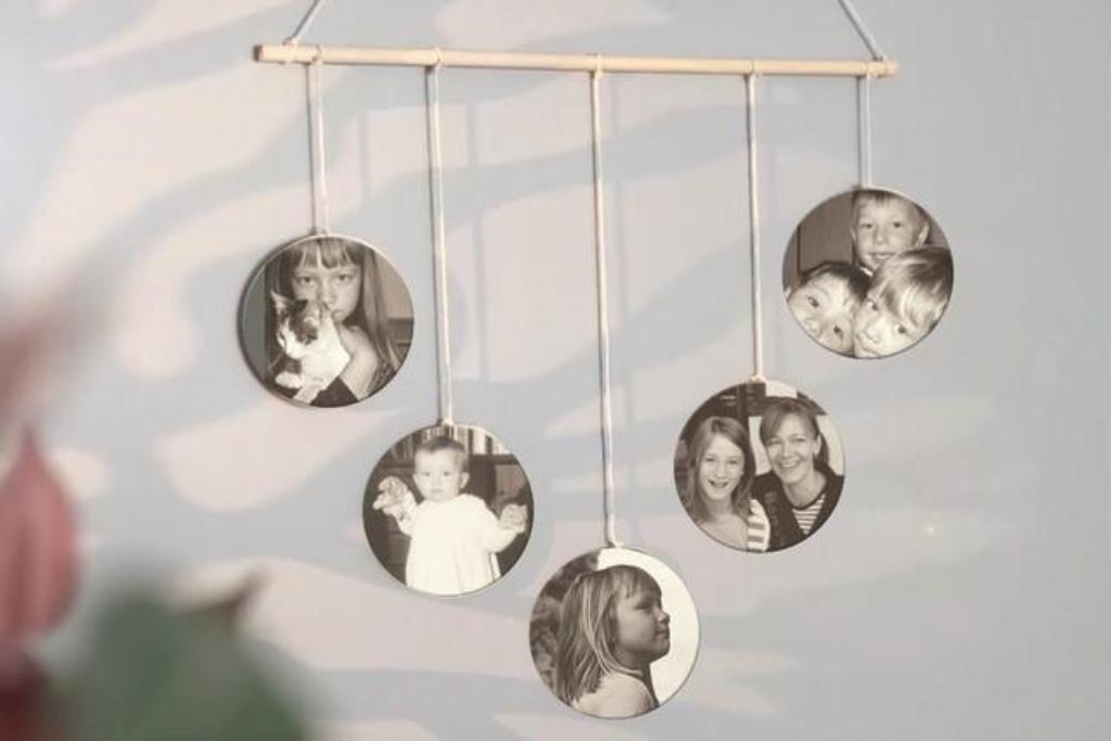 Fünf rund ausgeschnittene schwarz-weiße Fotos von Kindern und einer Frau hängen an Schnüren an einem Holzstab als Weihnachtsanhänger