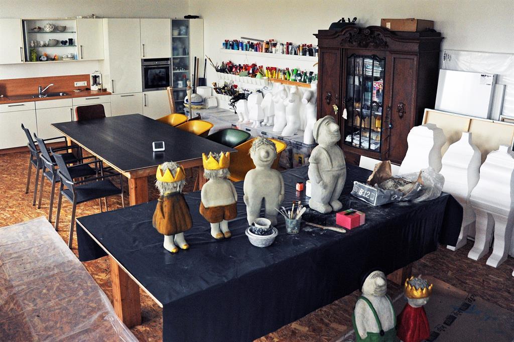 Atelier mit mehreren Figuren aus Ton oder Keramik auf Tischen und Regalen sowie Stühlen und einem antiken Schrank im Hintergrund