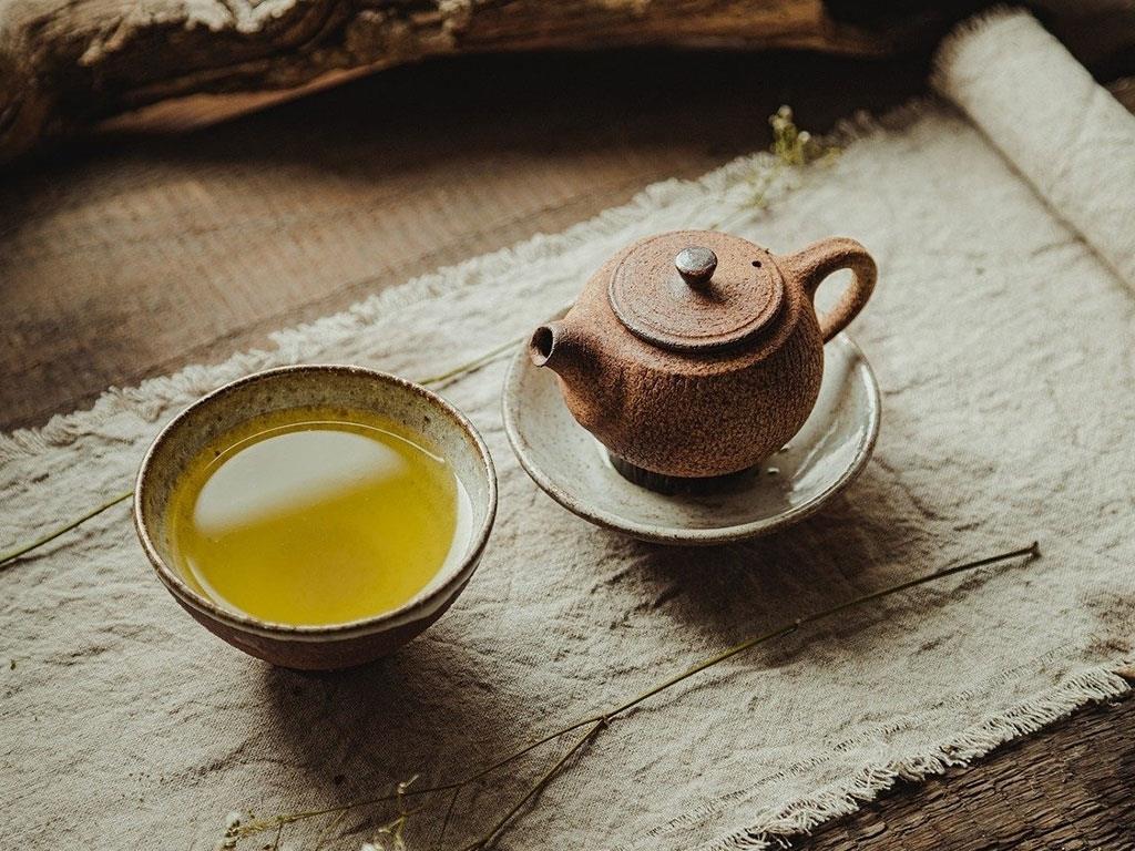 Eine steinernde Teekanne in einer Schale neben einer Schale Tee auf einem Holztisch stehend.