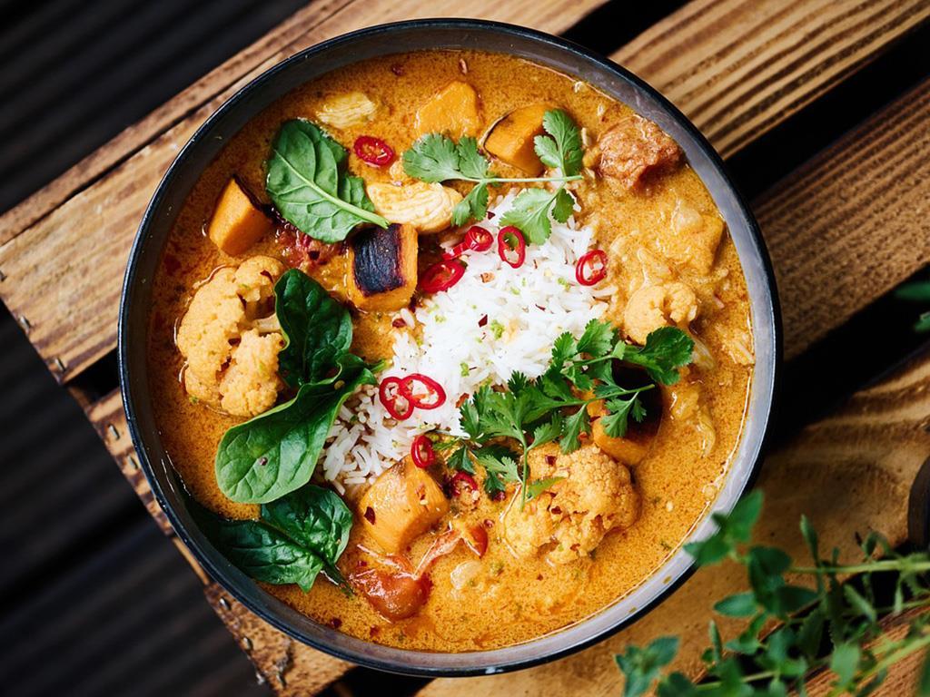 Eine Schüssel indisches Curry mit Blumenkohl, Tofu, Reis und verschiedenem Gemüse.