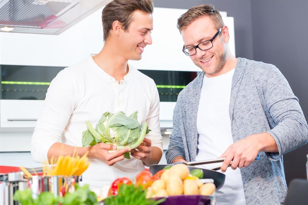 Zwei Männer kochen gemeisam Pasta mit verschiedenem Gemüse.