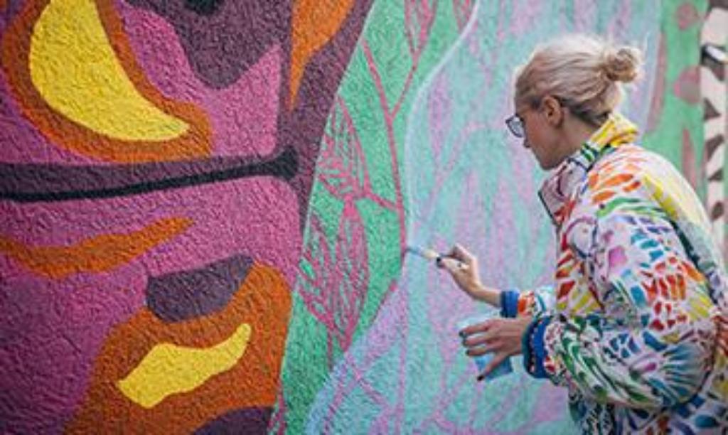 Kuenstlerin malt buntes Gemälde an eine Wand