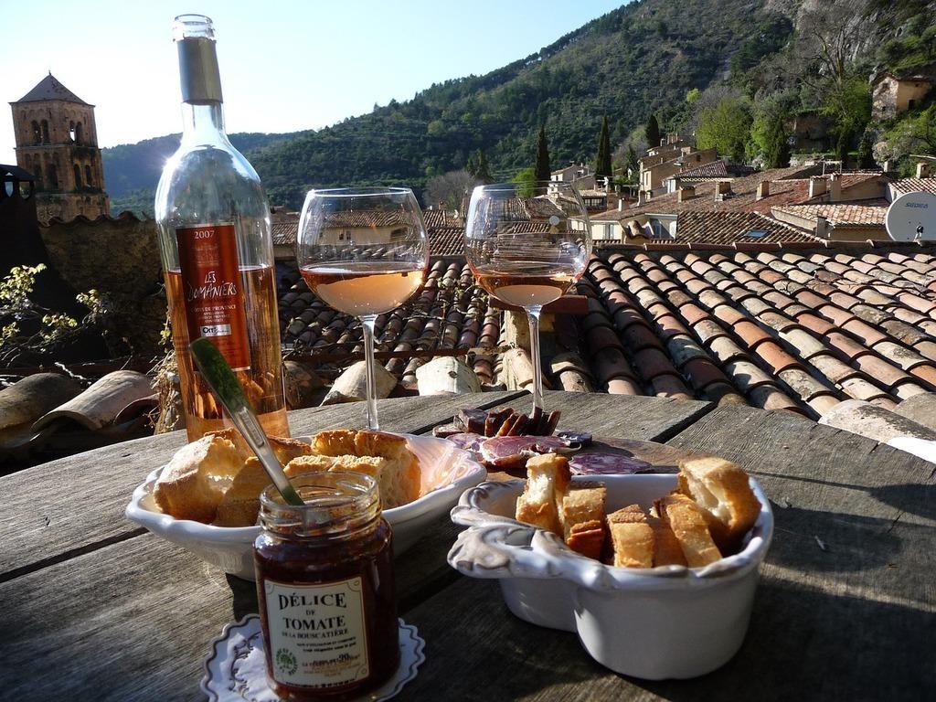 Tisch mit Flasche Roséwein, zwei Gläsern, Charcuterie und Brot mit Blick auf eine sonnige Landschaft