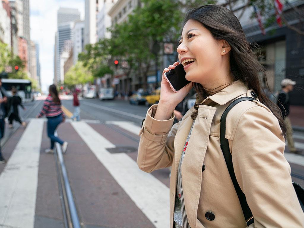 Eine Frau geht in der Stadt und telefoniert dabei mit ihrem Handy