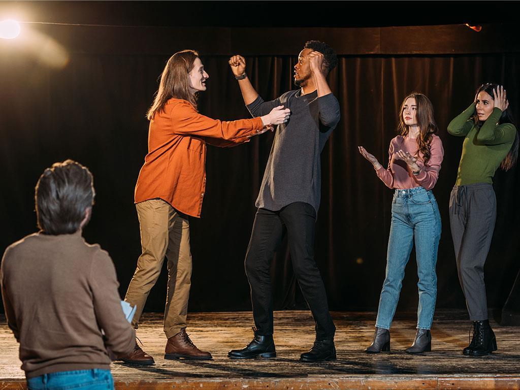 Eine Gruppe von Personen übt gemeinsam auf der Bühne eines Theaters