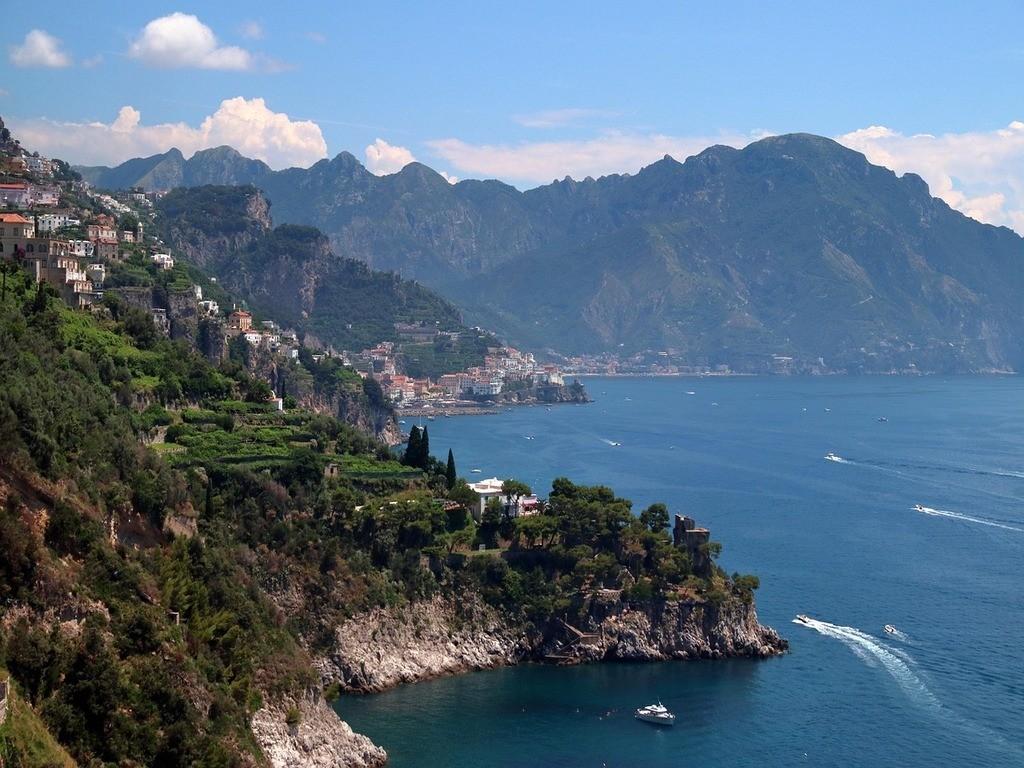 Typische sonnige Mittelmeerküste Italiens mit türkisblauem Meer, felsigen Klippen und mediterraner Landschaft.