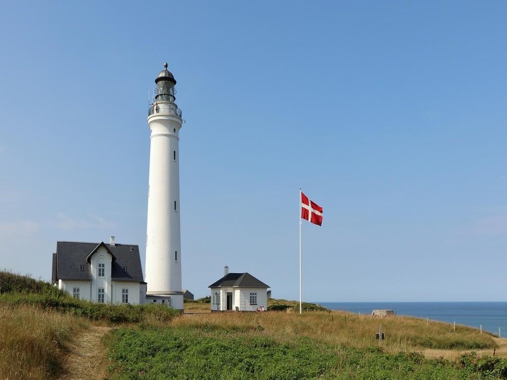 Weißer Leuchtturm an der dänischen Küste mit einer wehenden dänischen Flagge.